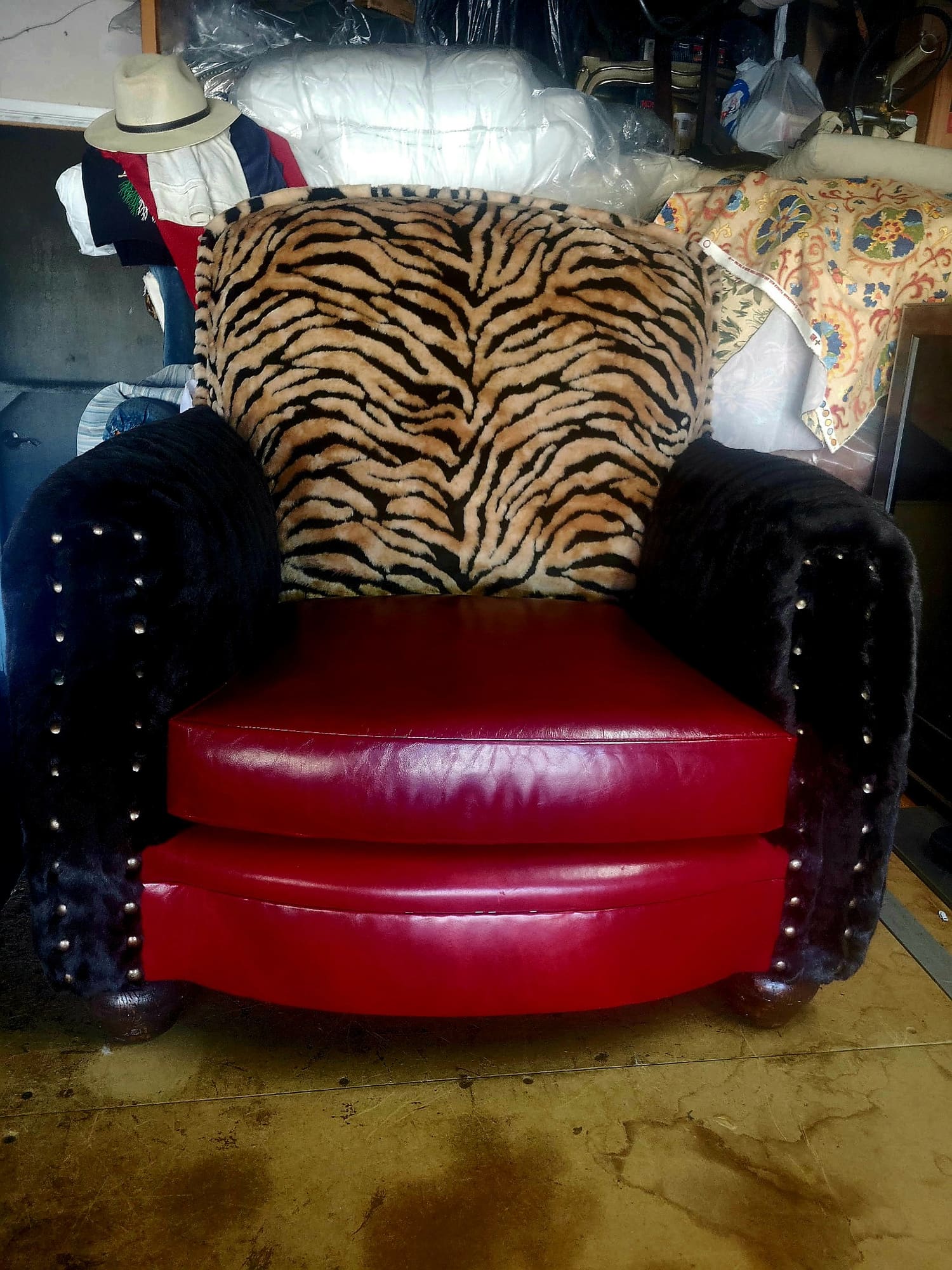 The finished club chair in the workshop: tiger-stripe plush back, black fur arms with brass nailheads, red leather seat